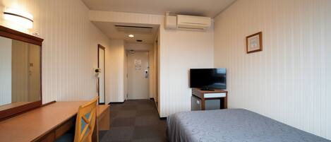 Een hotelkamer met een bed, een bureau, een stoel, een televisie en een airconditioner.