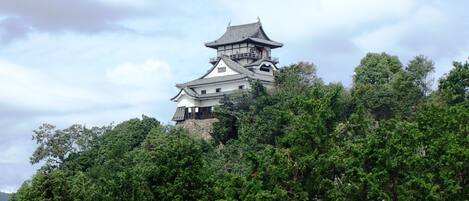 Een traditioneel Japans kasteel met meerdere verdiepingen en een opvallende centrale toren, omringd door weelderige groene begroeiing.