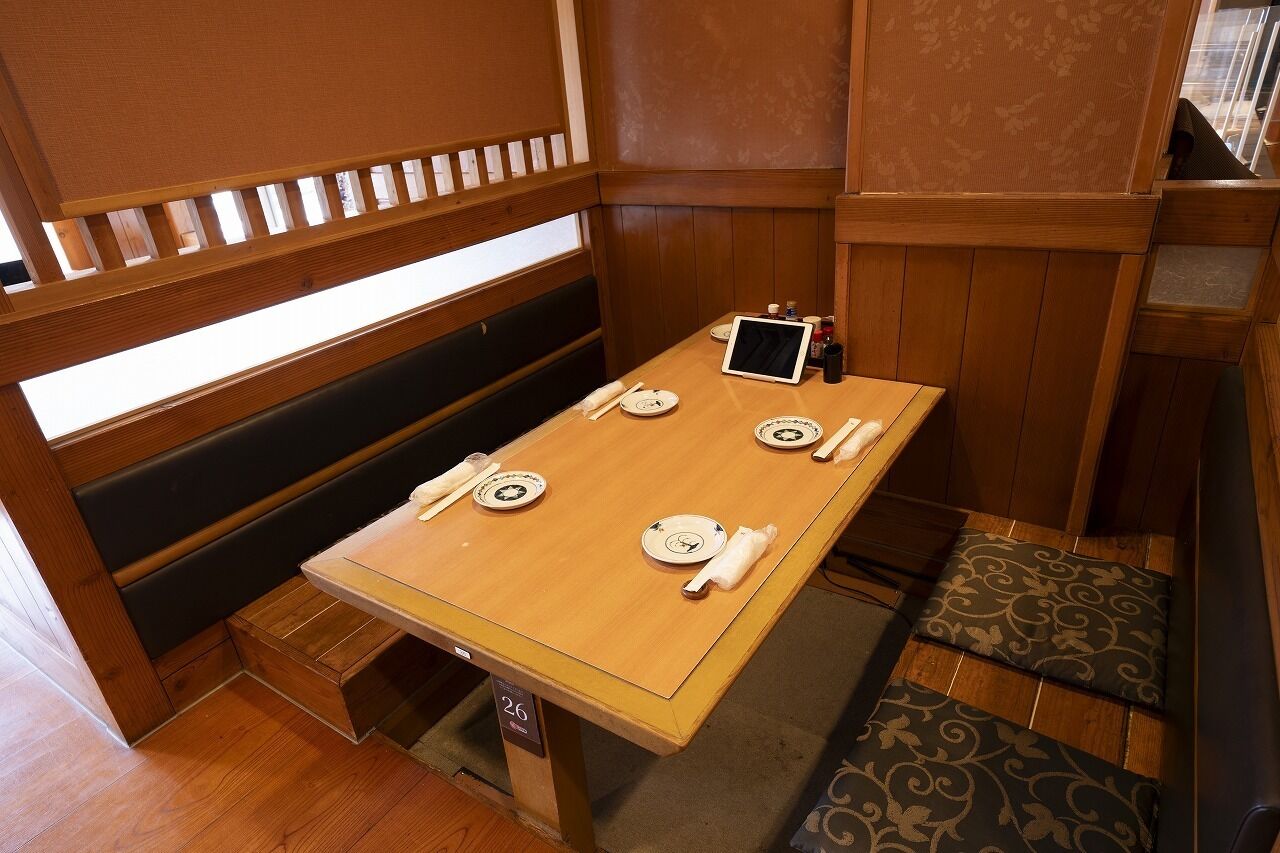 Una mesa de comedor de madera con platos, una tableta y un holder para servilletas en una habitación con paneles de madera y una ventana.