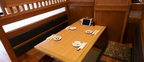 Una mesa de comedor de madera con platos, una tableta y un holder para servilletas en una habitación con paneles de madera y una ventana.