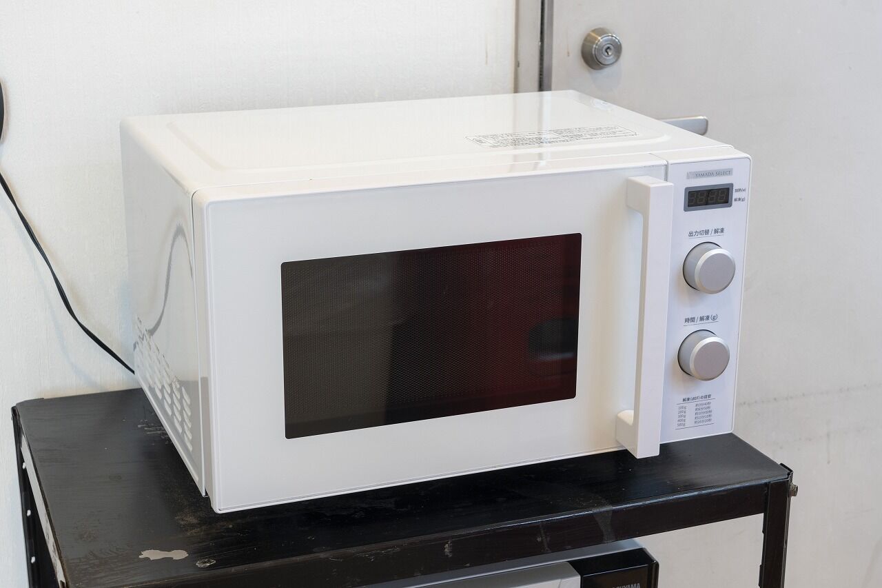 Un four à micro-ondes blanc est posé sur une table noire, devant un mur blanc.