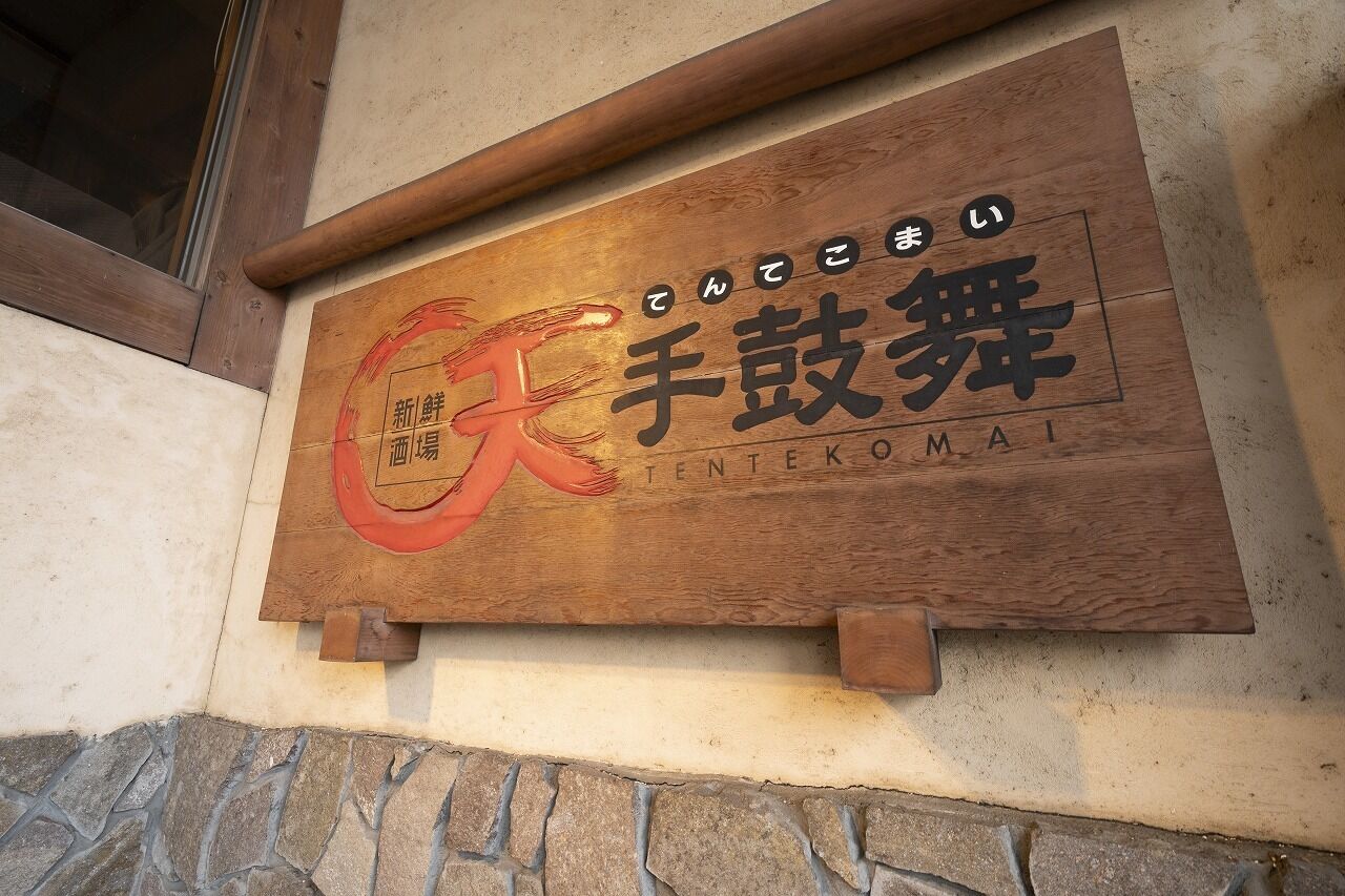 A wooden sign with Japanese characters and the name 'TENTEKOMAI' on a building facade.