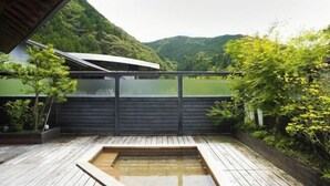A wooden deck with a hot tub, surrounded by lush greenery and a view of a lake and hills. - Auberge Tosayama (Kochi)