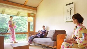 A room with a sofa, a standing chair, and a table. There is a window with a view of trees. - Auberge Tosayama (Kochi)