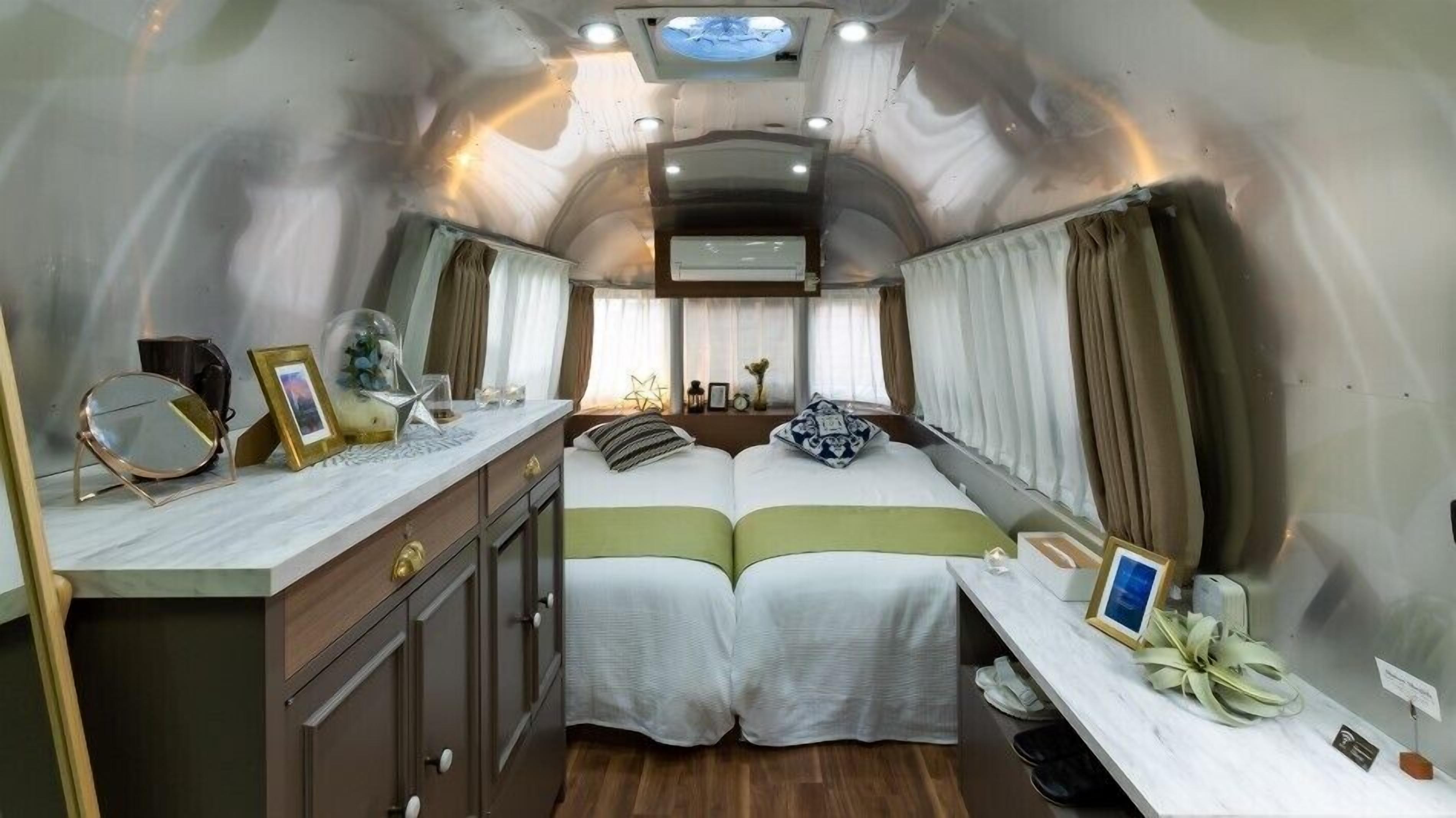 Un interior compacto y bien iluminado con cama, mesitas de noche y una pequeña zona de escritorio.