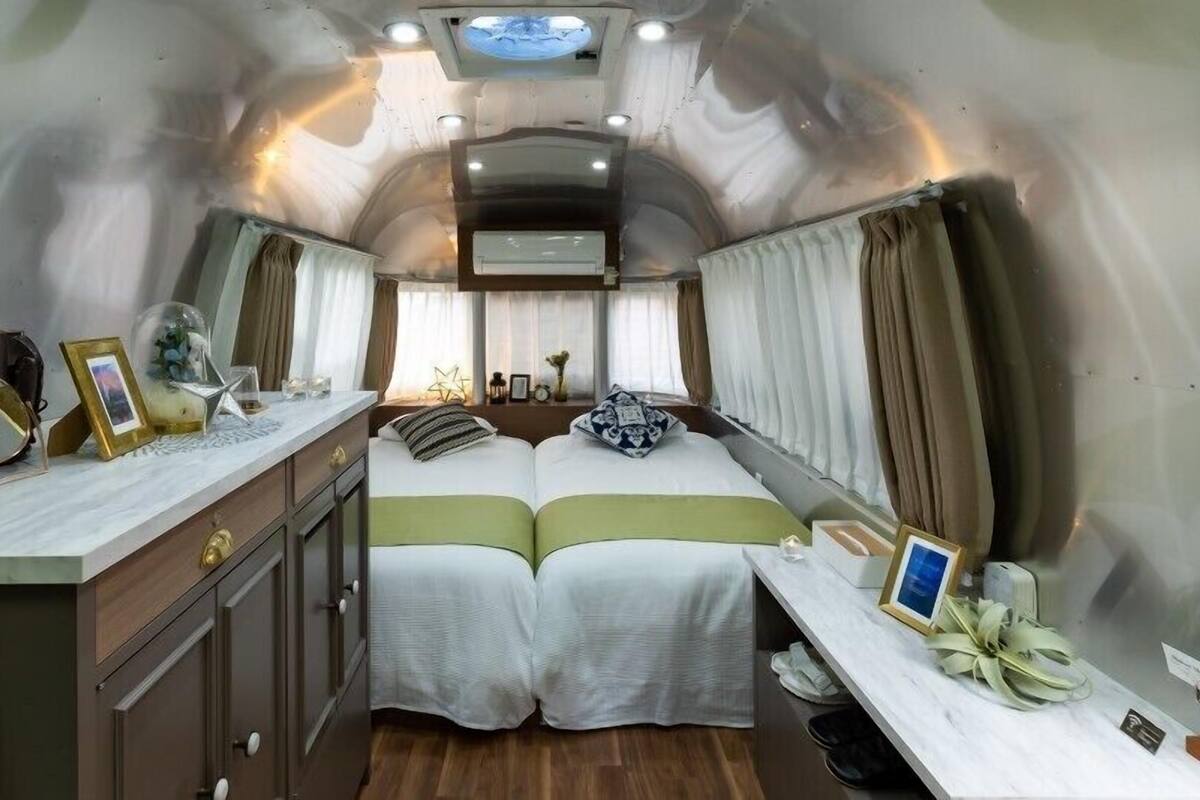 A compact, well-lit interior with a bed, bedside tables, and a small desk area.