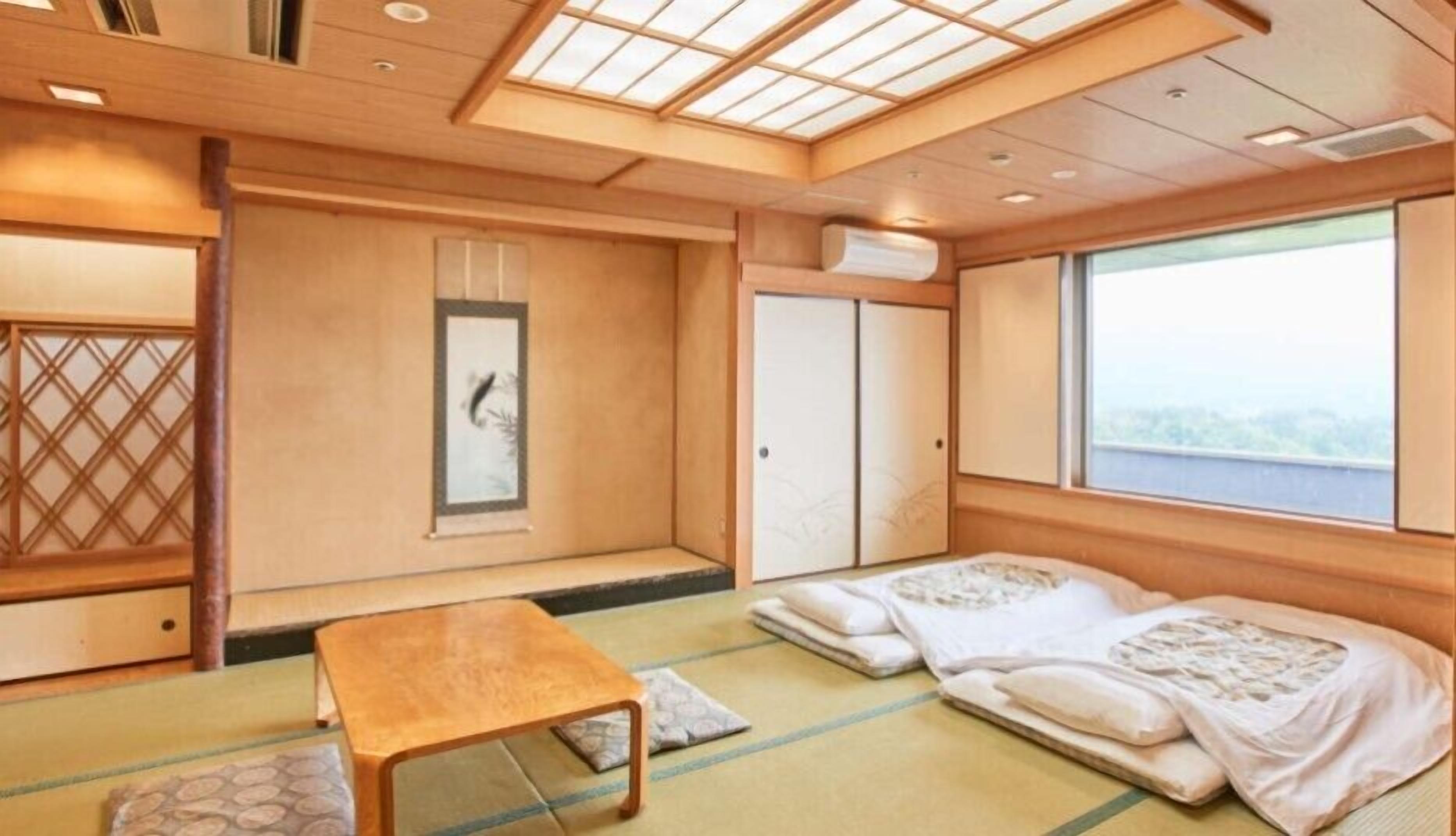 Una habitación japonesa tradicional con suelo de tatami, una mesa baja, puertas correderas y vistas a través de un ventanal grande.