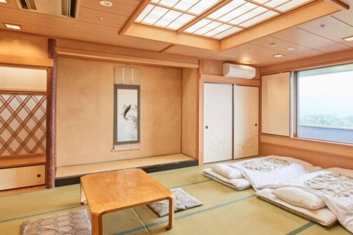 A traditional Japanese room with tatami flooring, a low table, sliding doors, and a view through a large window.