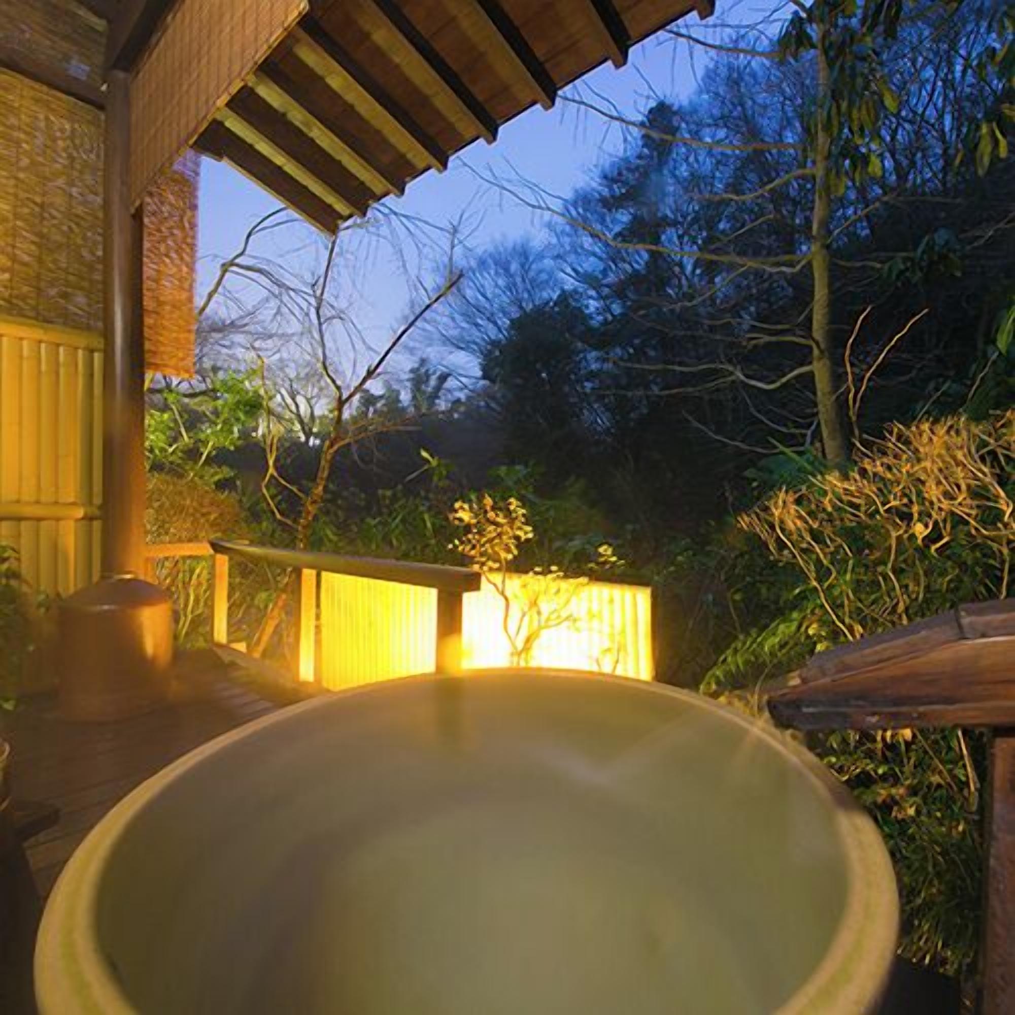 Uma banheira de hidromassagem em área externa coberta, com deck de madeira e parede de tijolos.