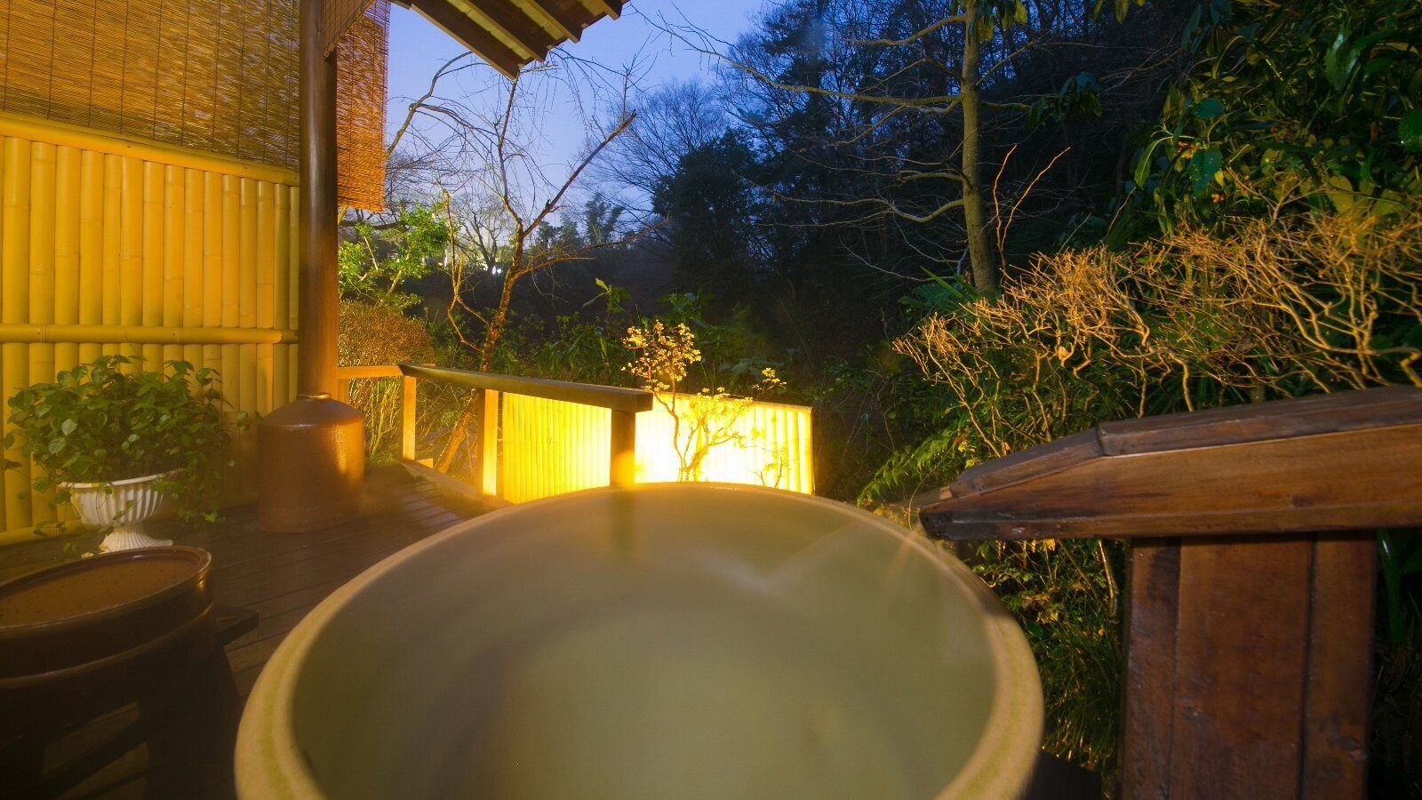 Un jacuzzi en un jardín con terraza de madera y valla de bambú.