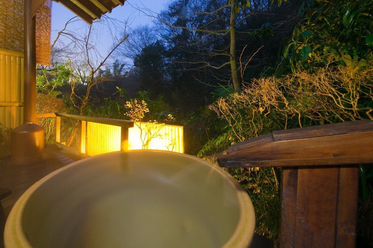 A hot tub in a garden with a wooden deck and a bamboo fence.