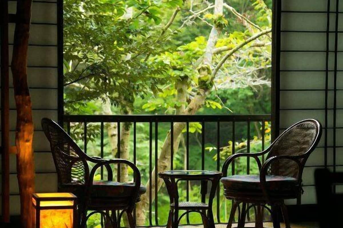 A balcony with two chairs and a table, a lantern, and a view of greenery.