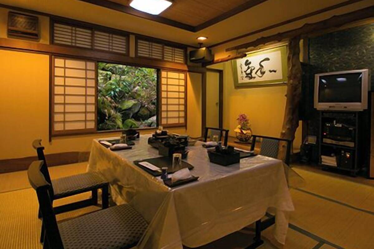 A traditional Japanese-style room with tatami flooring, a low table with cushions, a television, and a painting on the wall.
