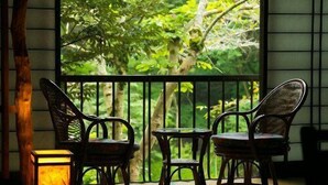 A balcony with two chairs and a table, a lantern, and a view of greenery. - Motoyu (Atsugi)