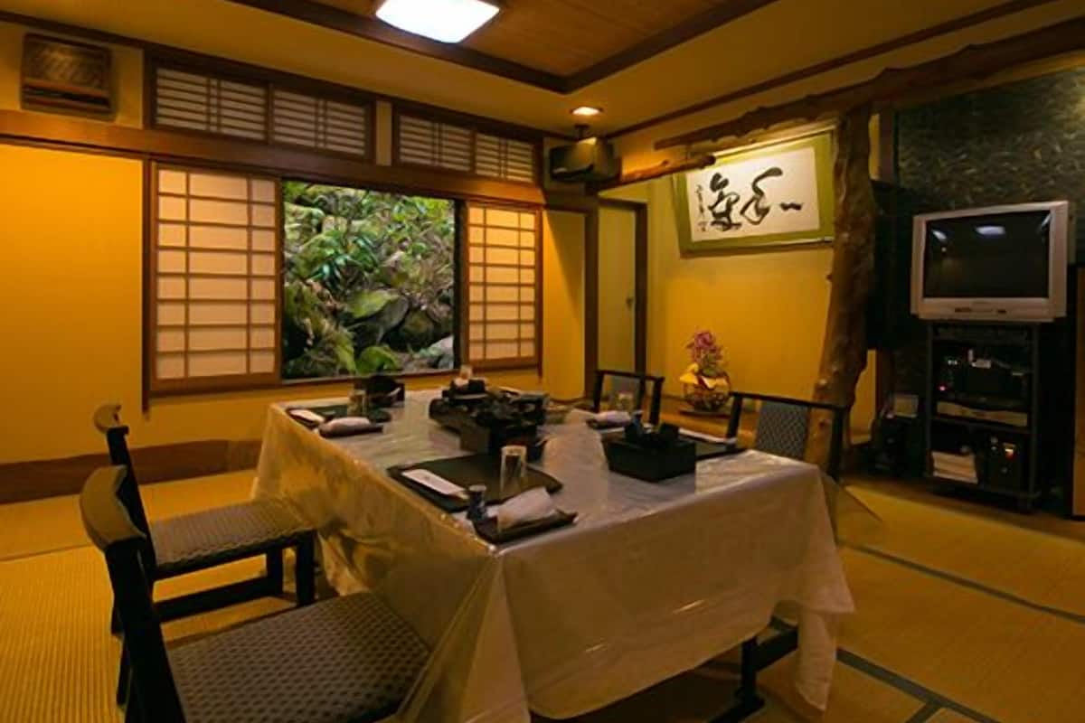 A traditional Japanese-style room with tatami flooring, a low table with a white tablecloth, and a television on a stand.
