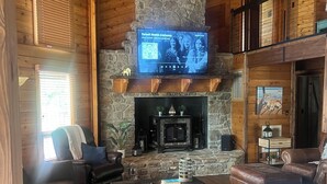 Een gezellige woonkamer met een stenen openhaard, leren banken en een flatscreen televisie erboven.