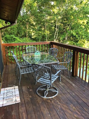 Enjoy a serene outdoor space with a deck overlooking a lush landscape, featuring a glass-top table and comfortable seating.
