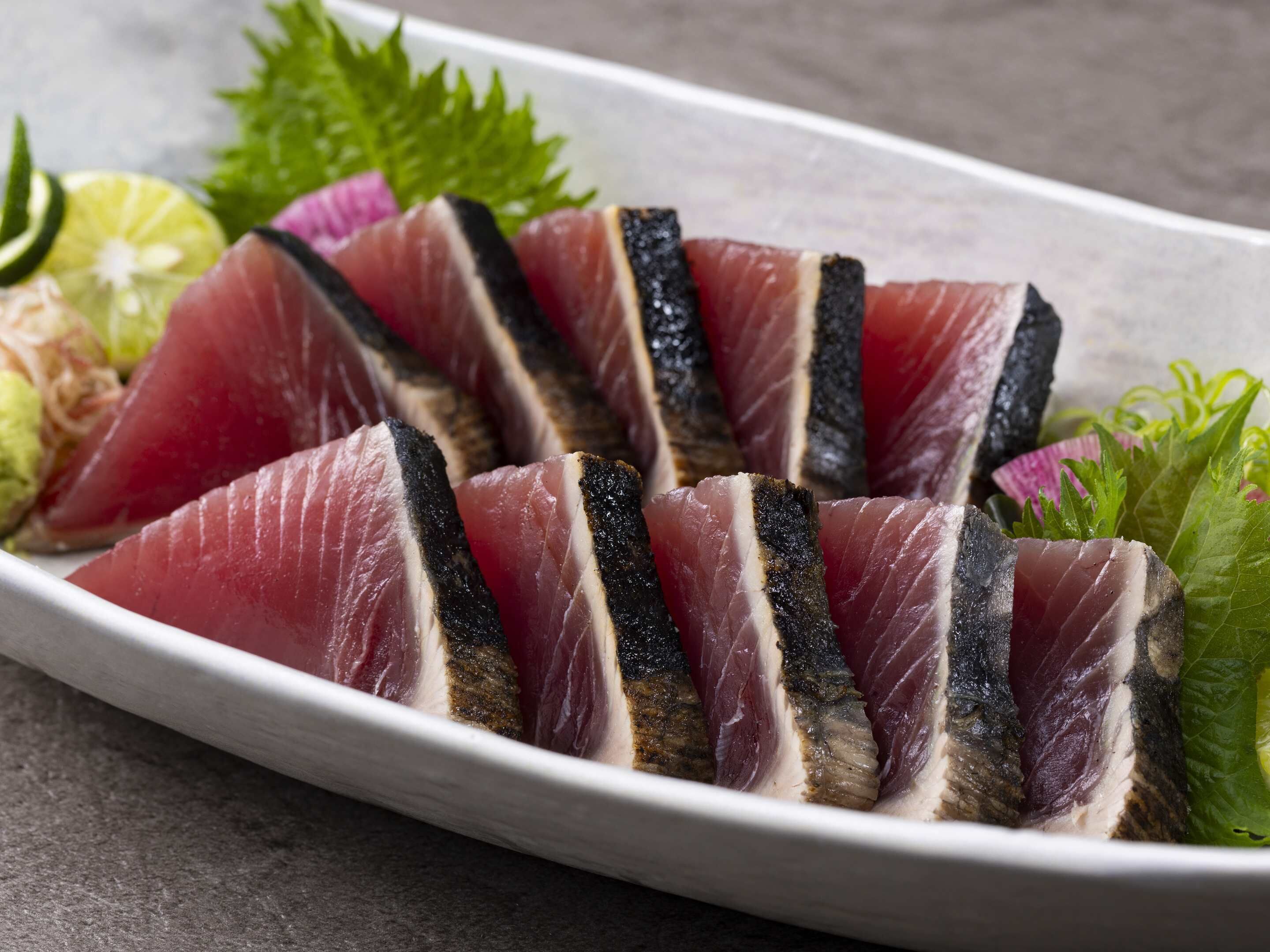 Een bord sashimi met groene bladeren en een partje limoen.