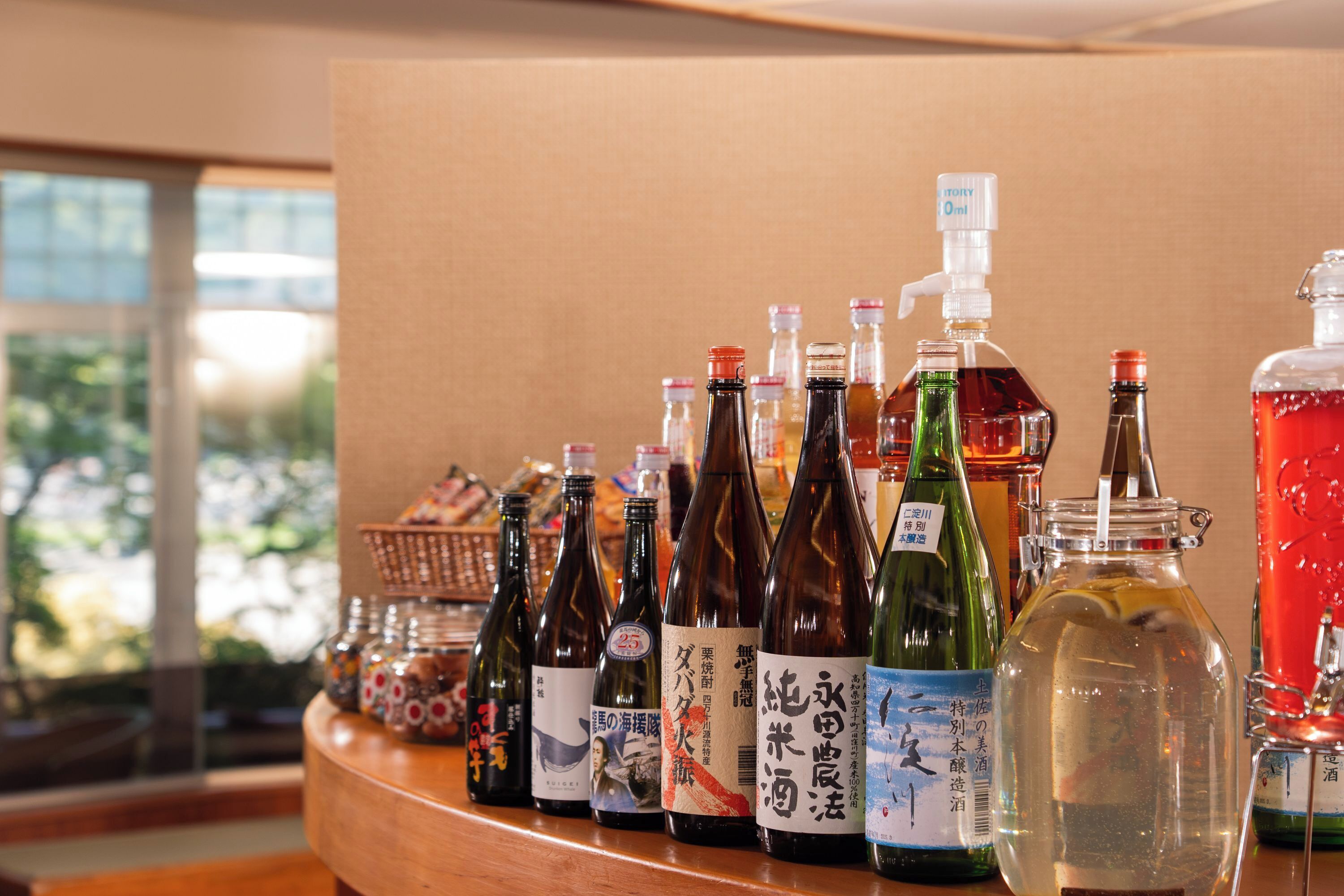 A variety of bottles with labels, likely containing beverages, arranged on a wooden counter.