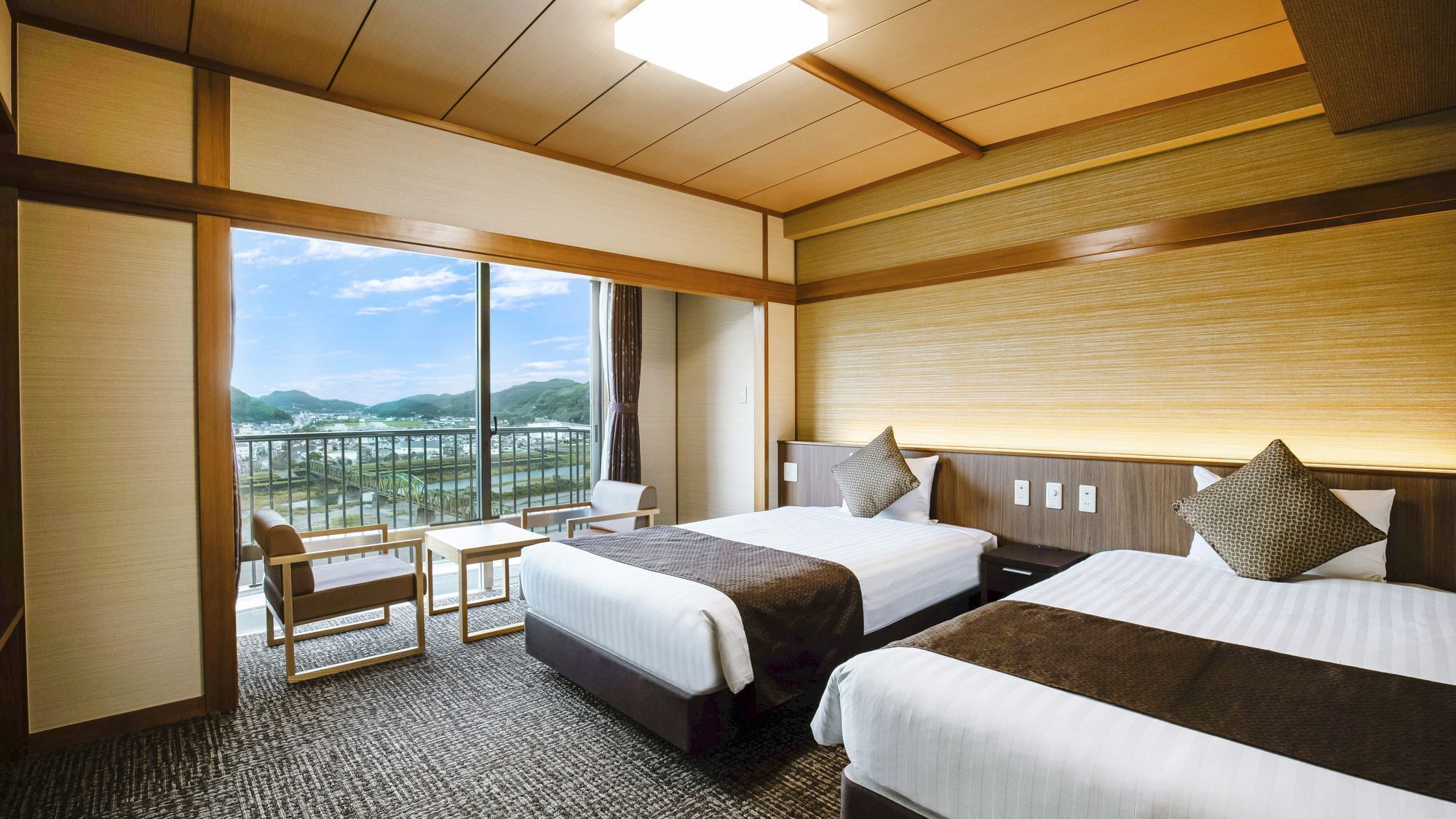 A hotel room with two beds, a seating area, and a large window offering a view of a bridge and landscape.