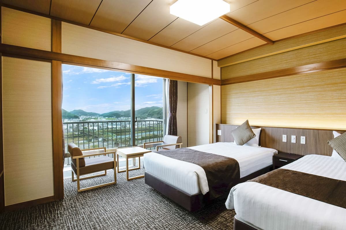 Une chambre d’hôtel avec deux lits, un coin salon et une grande fenêtre donnant sur un pont et un paysage.