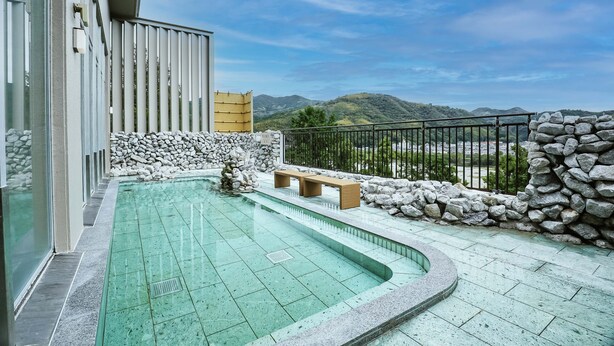Piscina con muro de piedra y banco, rodeada por una barandilla y vista a montañas.