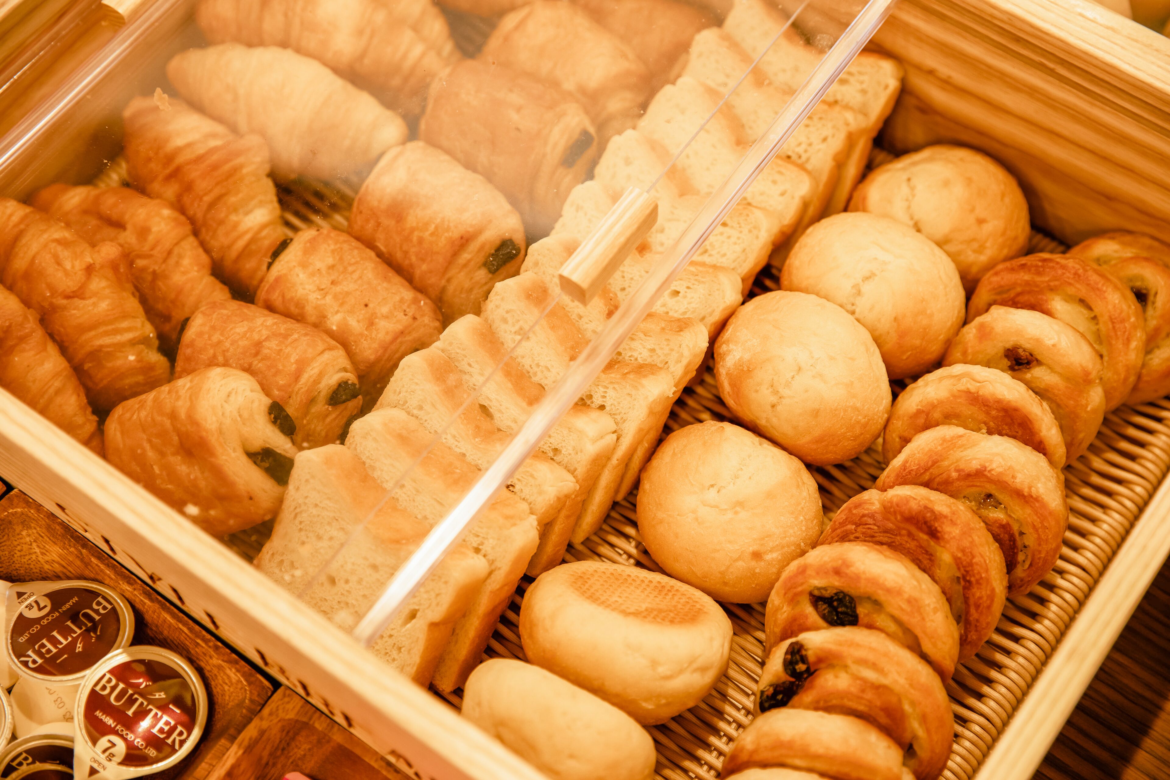 Eine Auslage mit verschiedenen Backwaren, darunter Croissants und Brötchen, angeordnet auf einer Holzschale.