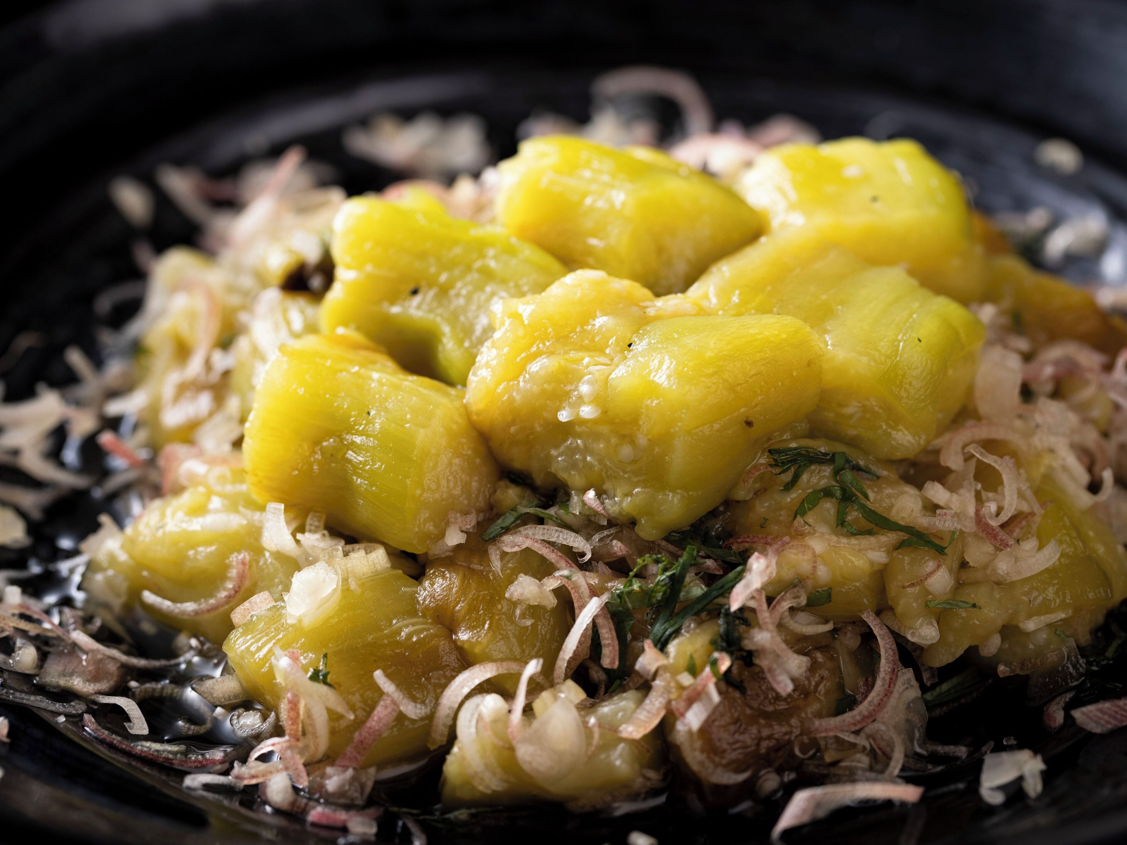 A close-up of a dish with yellow chunks, possibly potatoes, and thinly sliced onions, garnished with herbs.