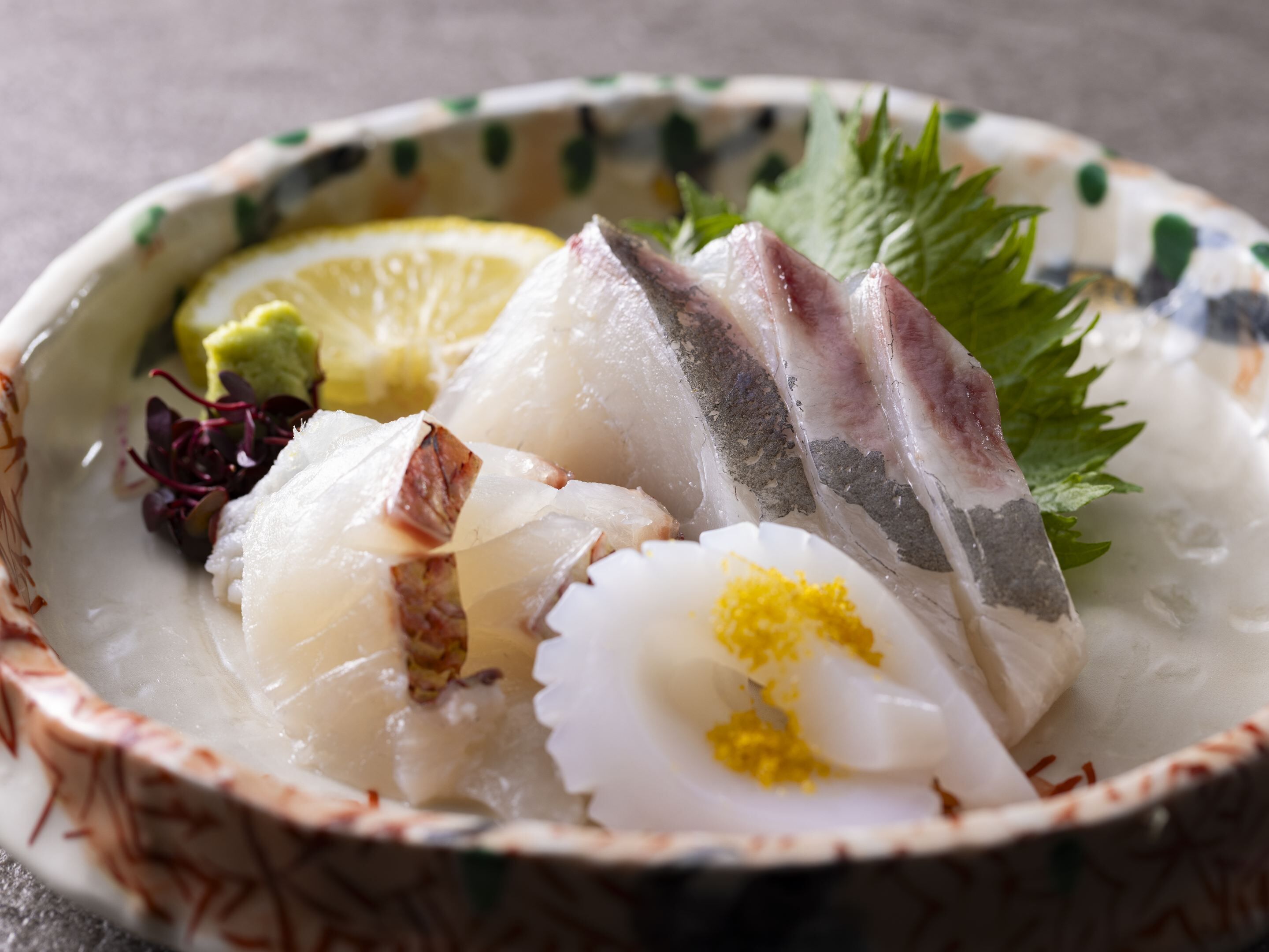A bowl of sashimi with lemon and greens.