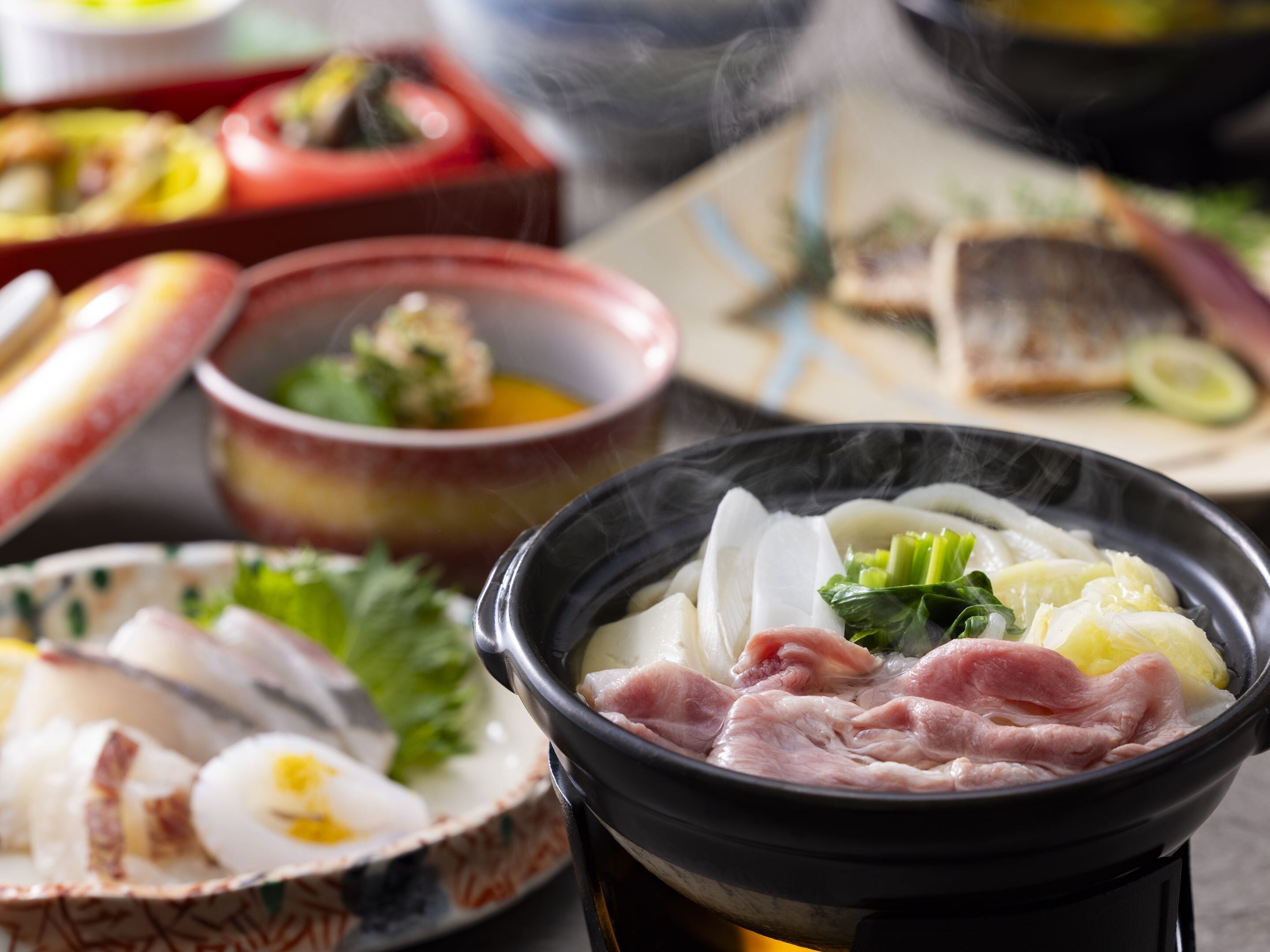 A variety of dishes including a hot pot with meat and vegetables, a bowl of soup, and other food items on a table.