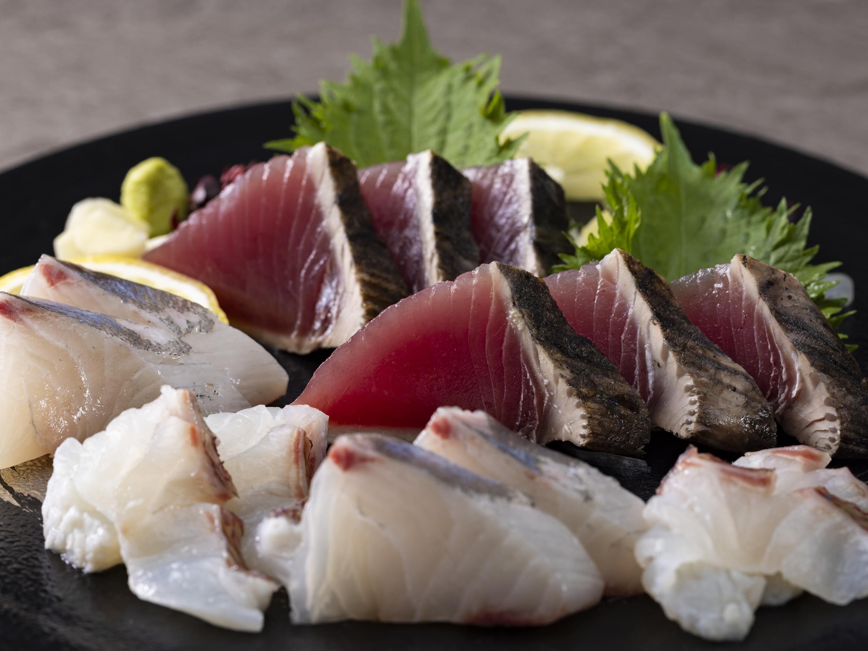 A plate of sashimi with various fish cuts, garnished with green leaves and lemon slices.
