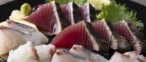 A plate of sashimi with various fish cuts, garnished with green leaves and lemon slices.