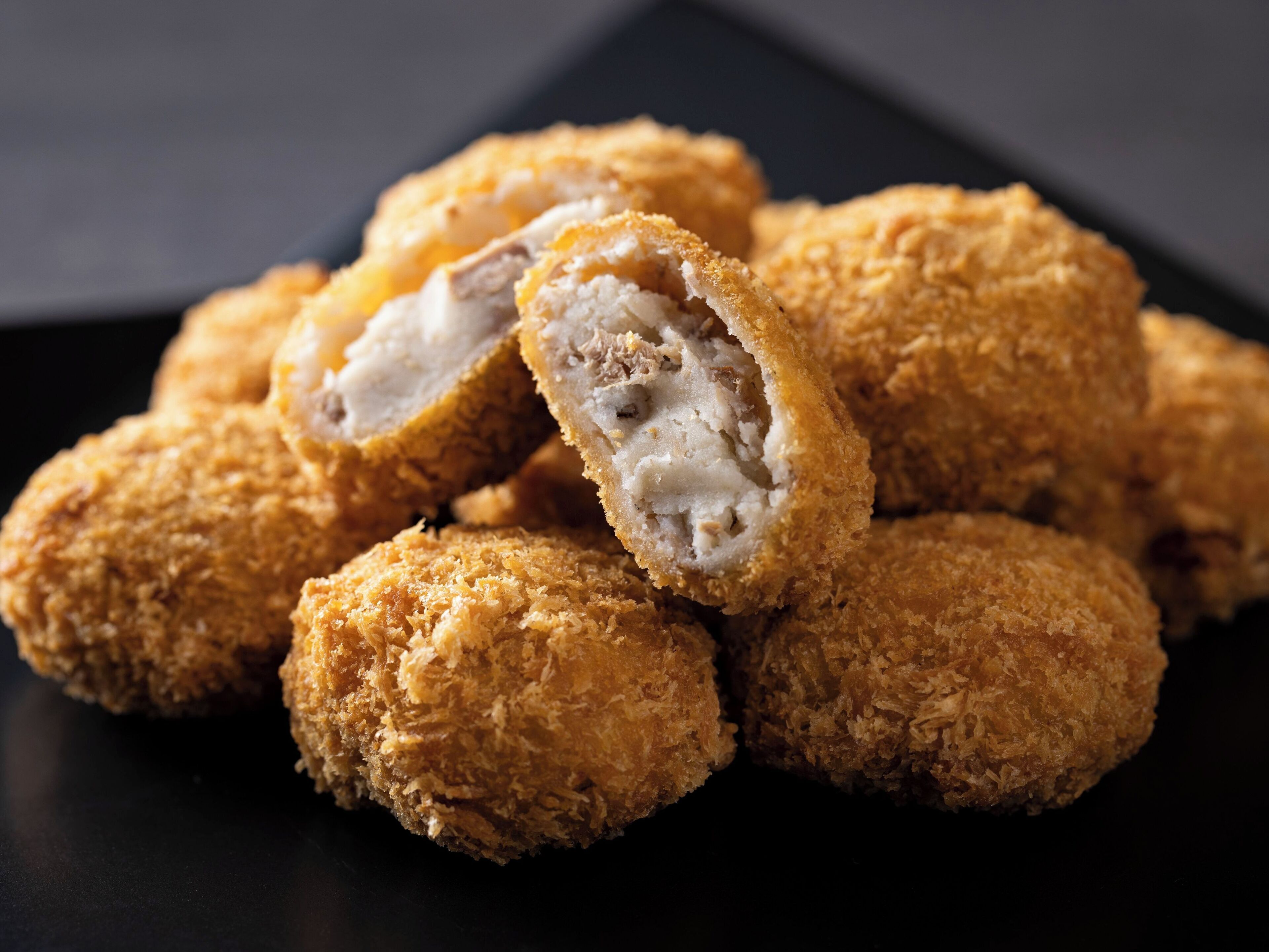 A pile of breaded and fried food items, likely croquettes, on a dark surface.