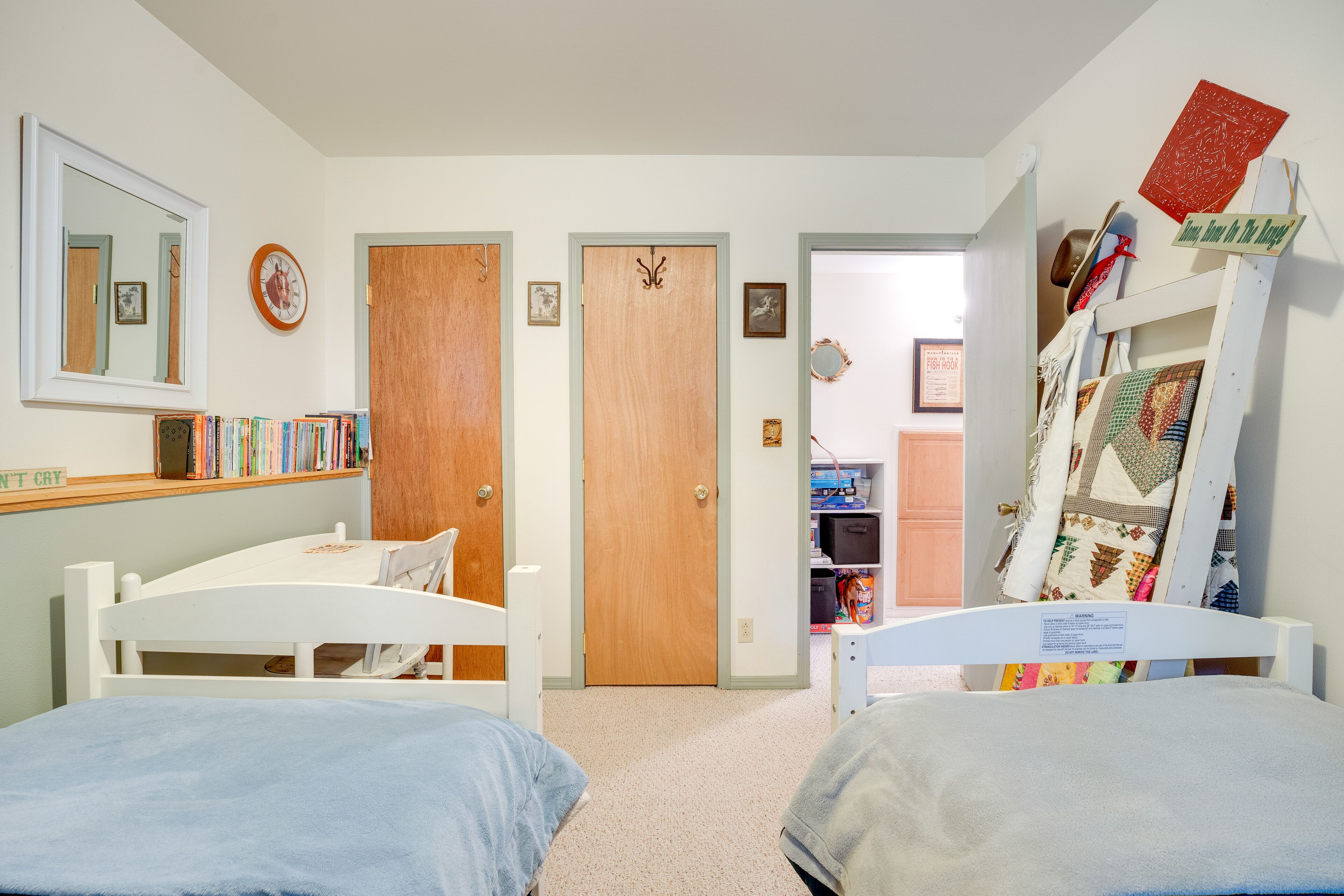 A bedroom with two single beds, a wooden door, a mirror, and a bookshelf.