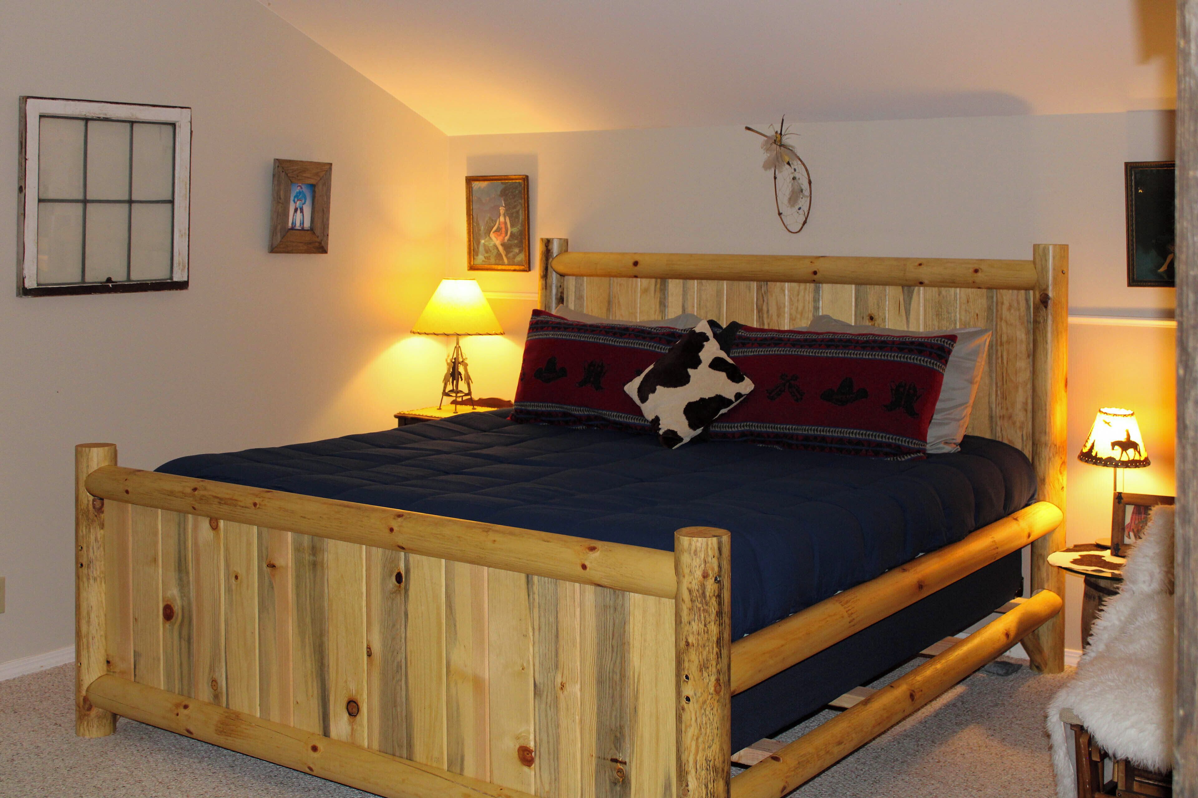 Ein hölzernes Bett mit blauer Matratze, einem Holz-Kopfteil und einem dekorativen Kissen. Eine Wandlampe und ein gerahmtes Bild sind an der Wand angebracht.
