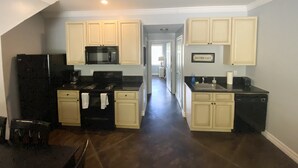 A kitchen with white cabinets, a black refrigerator, a microwave, a stove, and a sink.