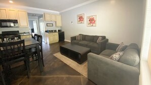 A spacious living room with a grey sofa, a dining table with chairs, and a kitchen in the background.