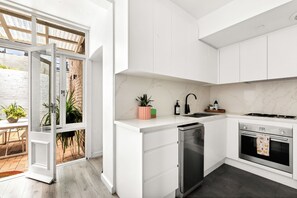 A modern kitchen with white cabinetry, a dishwasher, a stove, and a sink. - Renovated 3BR Heritage Home  | Private Veranda walk to the Rocks and  Barangaroo (Millers Point)