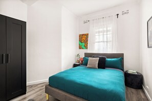 A bedroom with a bed, a wardrobe, a nightstand, a window with curtains, and a wall-mounted artwork. - Renovated 3BR Heritage Home  | Private Veranda walk to the Rocks and  Barangaroo (Millers Point)