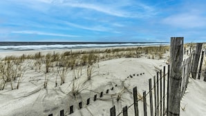 Ein Sandstrand mit einer Holzzaun und vereinzelter Vegetation.