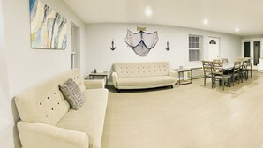 A living room with a beige sofa, a coffee table, and a dining area with a table and chairs. There is a wall decoration with anchors and the word "Relax". - 304 3rd Street, Suite A (Watkins Glen)