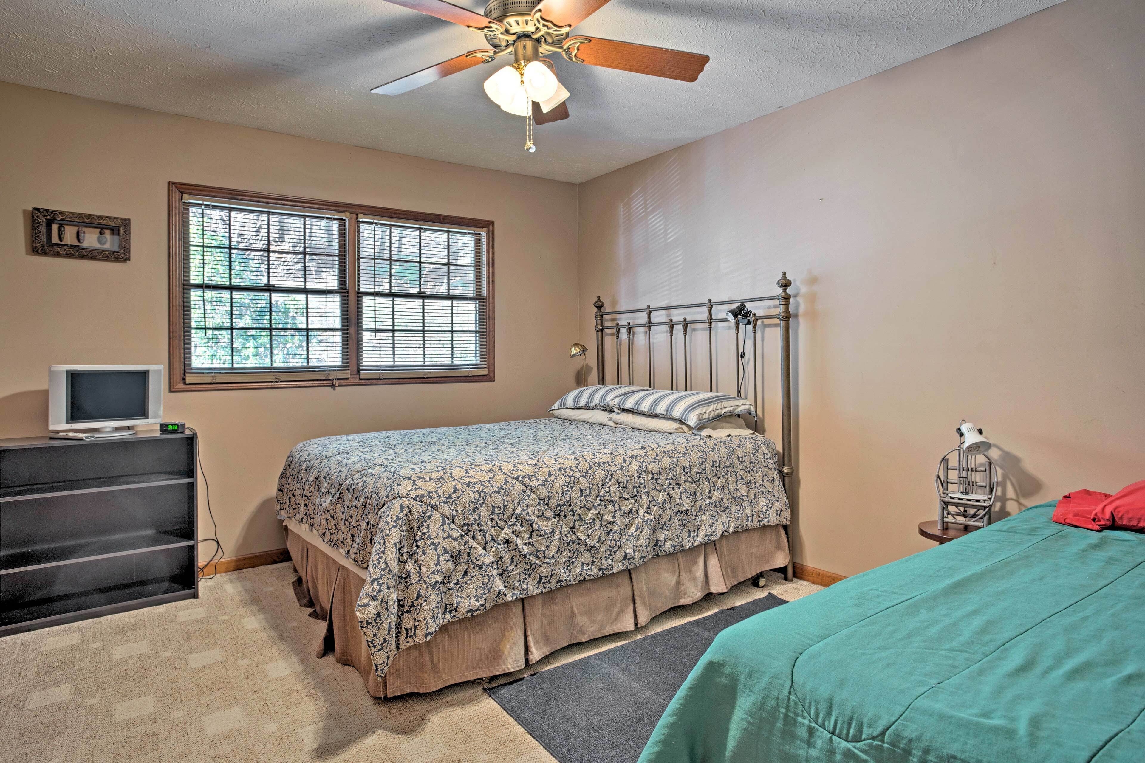 A bedroom with a bed, a desk with a computer, a window with blinds, and a ceiling fan.