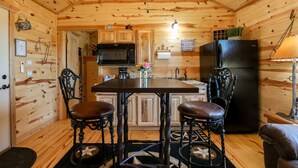 Une cuisine chaleureuse, aménagée dans le style d’un chalet, avec des murs en bois, un îlot central, deux chaises, un réfrigérateur et un four à micro-ondes.