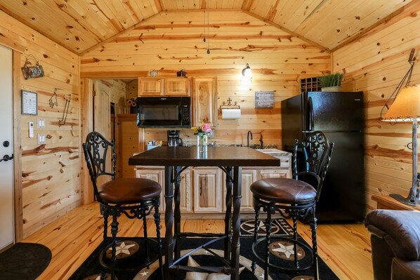 A cozy cabin-style kitchen with wooden walls, a central island, two chairs, a refrigerator, and a microwave.