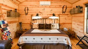 Une chambre confortable dans un chalet en rondins, avec un lit, une courtepointe, une tête de lit en bois et un ventilateur de plafond.