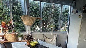 Una cocina con una amplia mesa blanca, una lámpara de macramé colgante y vistas a la vegetación a través de las ventanas.