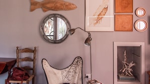 Una habitación con un espejo redondo, adorno de pez de madera, una obra de arte enmarcada y una lámpara.