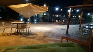 Un'area patio esterna con pavimento in pietra, sedie in metallo, un tavolo e un ampio ombrellone.