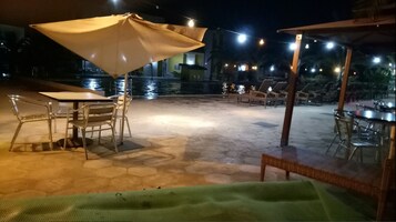 An outdoor patio area with stone flooring, metal chairs, a table, and a large umbrella.