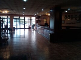 A spacious lobby with a reception desk, a large window, and a tiled floor.